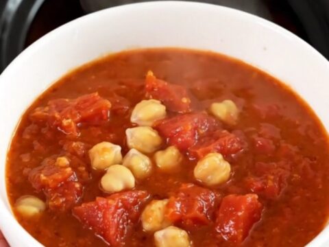 A top-down view of a black slow cooker filled with chickpeas, carrots, and tomato pulp before cooking.