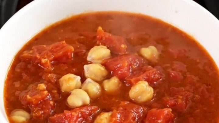 A top-down view of a black slow cooker filled with chickpeas, carrots, and tomato pulp before cooking.
