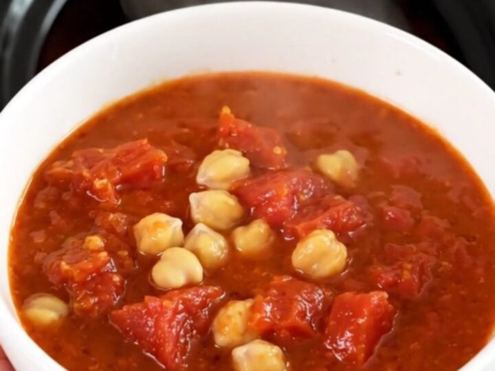 A top-down view of a black slow cooker filled with chickpeas, carrots, and tomato pulp before cooking.