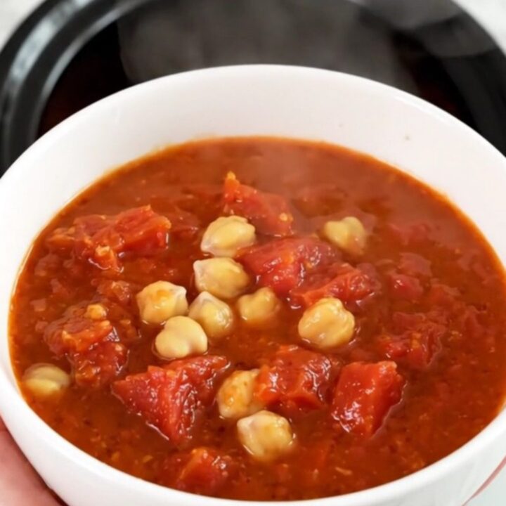 A top-down view of a black slow cooker filled with chickpeas, carrots, and tomato pulp before cooking.