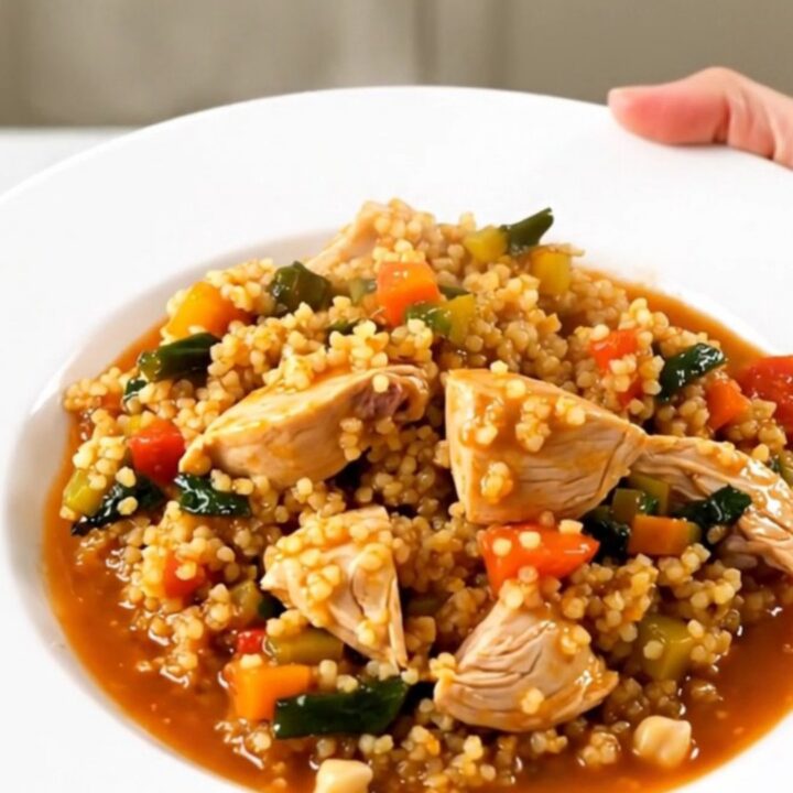 A slow cooker filled with chicken thighs, carrots, turnips, and chickpeas in a rich, glossy tomato-based sauce.