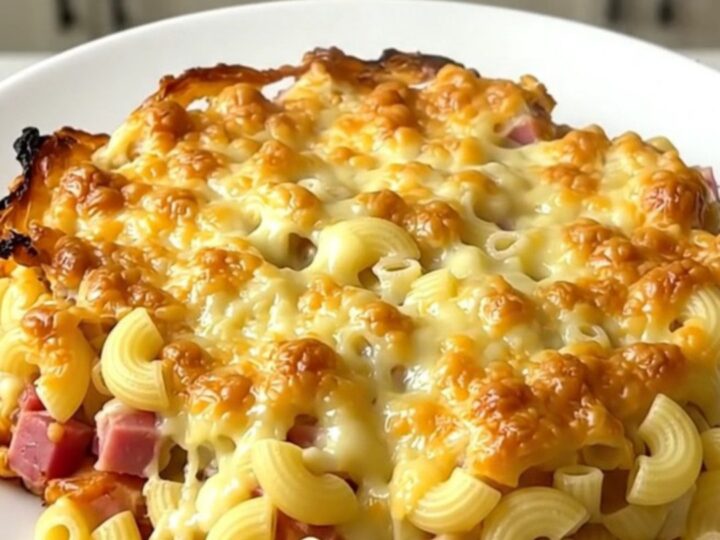 A top-down view into a black slow cooker filled with a creamy, golden-brown ham and macaroni gratin.