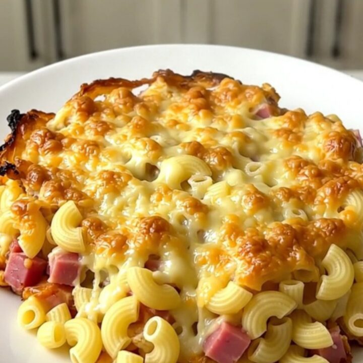 A top-down view into a black slow cooker filled with a creamy, golden-brown ham and macaroni gratin.