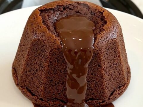 A warm, molten dark chocolate fondant on a white plate with a glossy, flowing center.