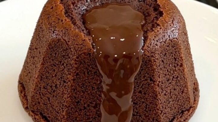 A warm, molten dark chocolate fondant on a white plate with a glossy, flowing center.
