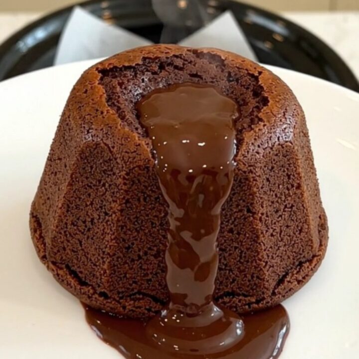 A warm, molten dark chocolate fondant on a white plate with a glossy, flowing center.