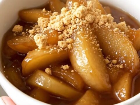 A white bowl filled with glossy, steaming apple and pear compote, garnished with crumbled biscuits.