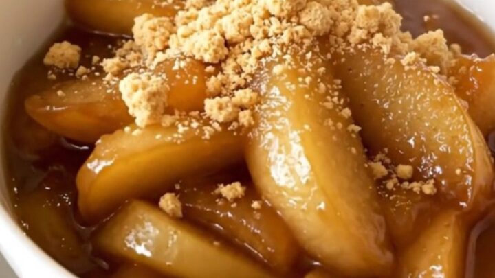 A white bowl filled with glossy, steaming apple and pear compote, garnished with crumbled biscuits.