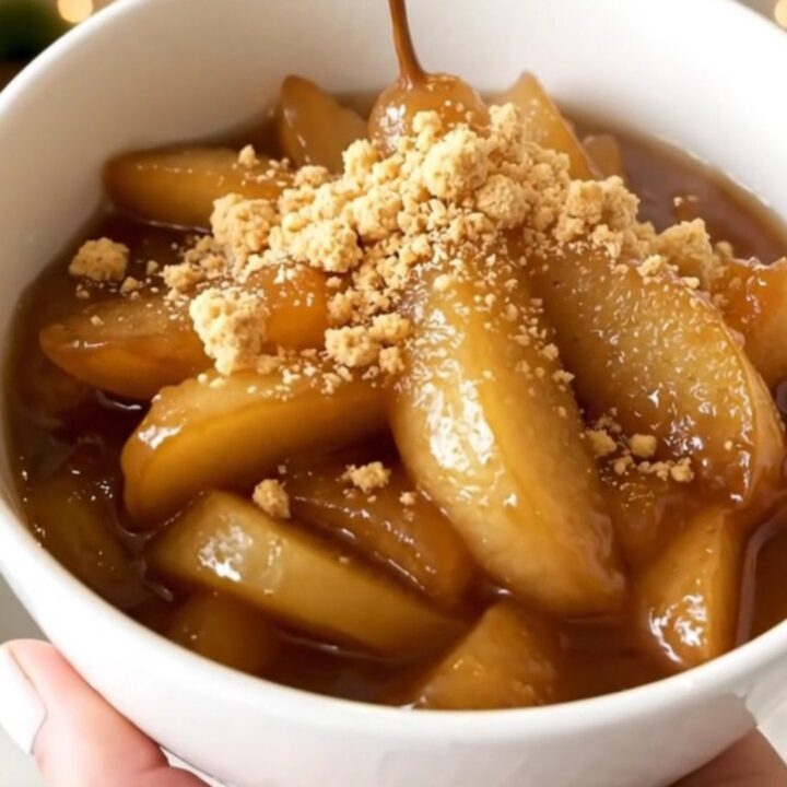 A white bowl filled with glossy, steaming apple and pear compote, garnished with crumbled biscuits.