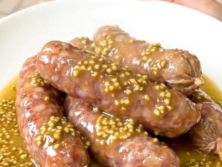 A close-up of slow-cooked andouillettes smothered in a creamy mustard and white wine sauce with mushrooms.