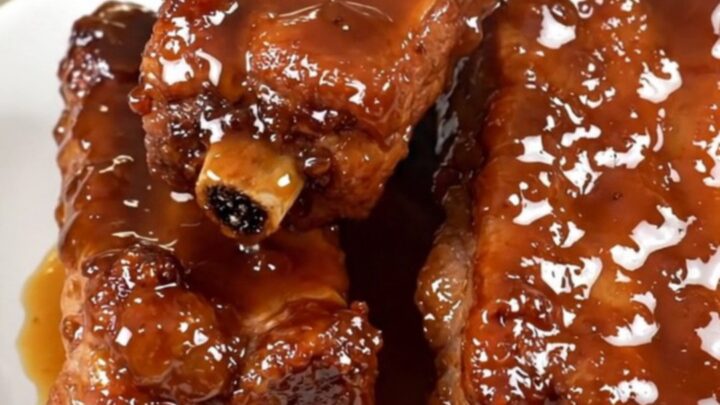 A plate of sticky, glazed slow-cooked pork ribs with a deep brown honey-soy coating.