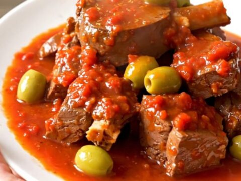 A bowl of tender veal stew with green olives in a rich tomato sauce.