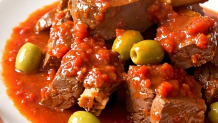 A bowl of tender veal stew with green olives in a rich tomato sauce.