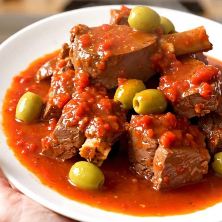 A bowl of tender veal stew with green olives in a rich tomato sauce.