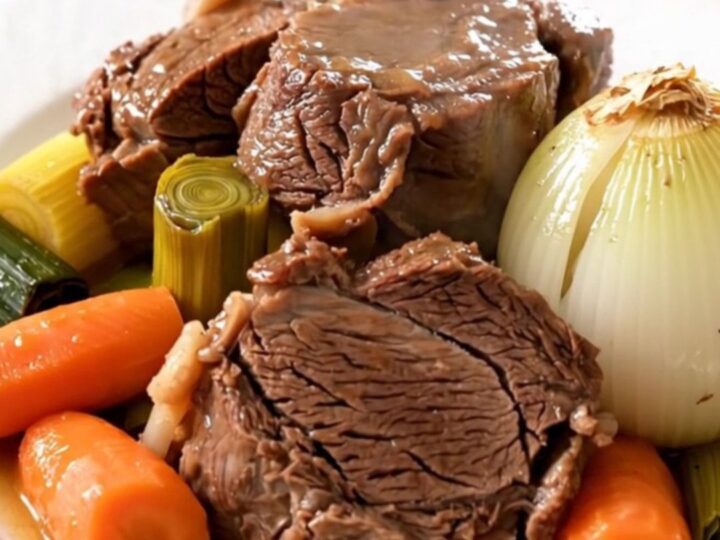 A slow cooker filled with a beef shank, carrots, leeks, and turnips in a savory broth.
