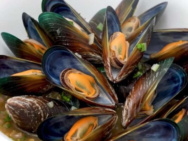 A top-down view of fresh raw mussels, sliced shallots, and herbs arranged in a slow cooker insert before cooking.