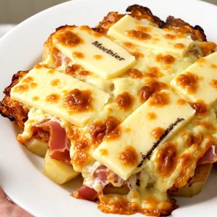 A top-down view of a slow cooker filled with layers of potatoes, bacon, and slices of Morbier cheese.