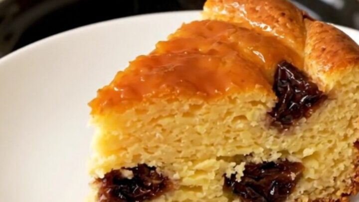 A golden-brown slice of Far Breton on a white plate, steaming slightly with visible prunes inside.