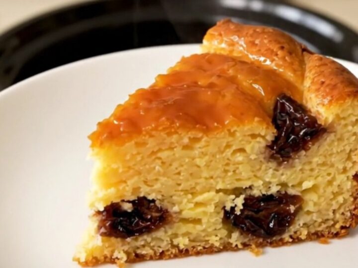 A golden-brown slice of Far Breton on a white plate, steaming slightly with visible prunes inside.