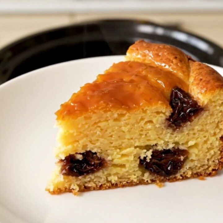 A golden-brown slice of Far Breton on a white plate, steaming slightly with visible prunes inside.