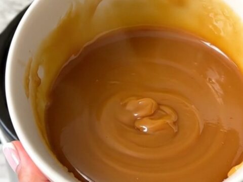 Un bol blanc rempli de caramel au beurre salé brillant et onctueux avec une texture lisse.