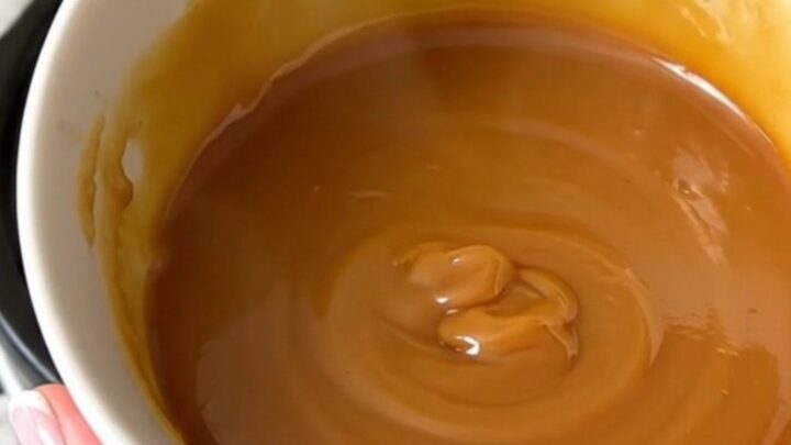Un bol blanc rempli de caramel au beurre salé brillant et onctueux avec une texture lisse.