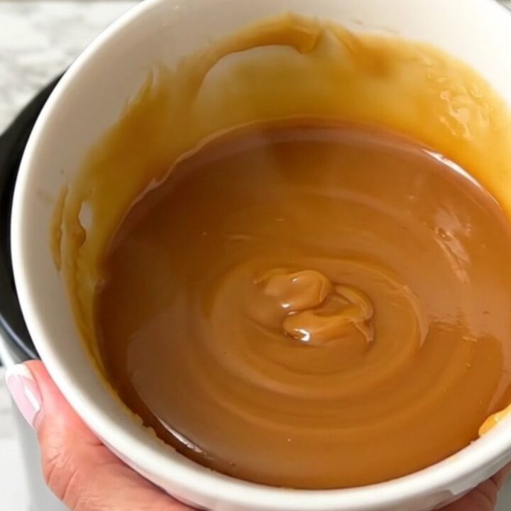 Un bol blanc rempli de caramel au beurre salé brillant et onctueux avec une texture lisse.