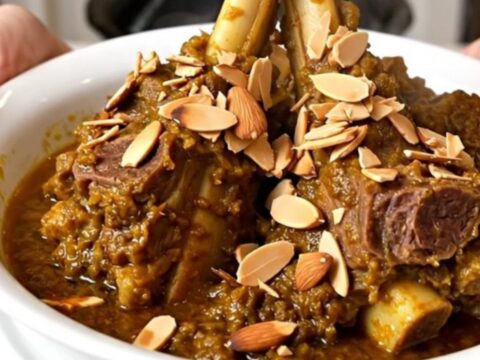 A top-down view of a slow cooker filled with lamb, prunes, and onions in a spiced broth.