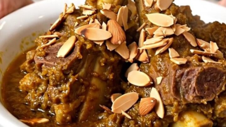 A top-down view of a slow cooker filled with lamb, prunes, and onions in a spiced broth.