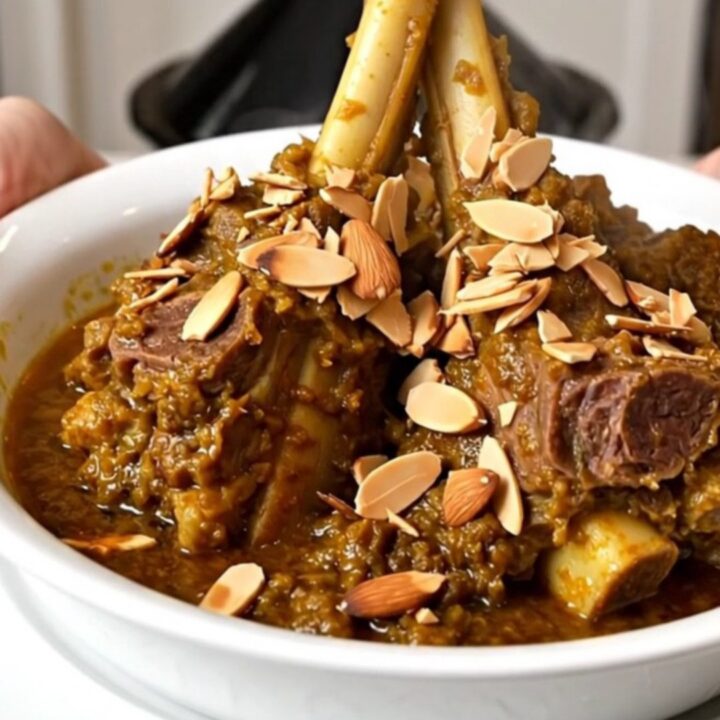 A top-down view of a slow cooker filled with lamb, prunes, and onions in a spiced broth.