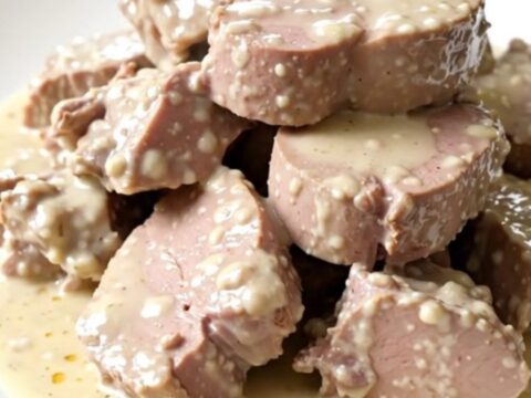 A top-down view of a slow cooker filled with raw veal, leeks, mushrooms, and carrots on a speckled countertop.