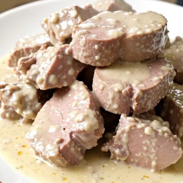 A top-down view of a slow cooker filled with raw veal, leeks, mushrooms, and carrots on a speckled countertop.