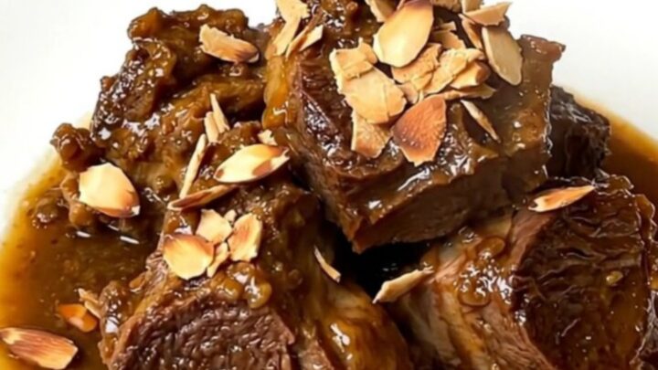 A close-up of slow-cooked tender lamb chunks in a rich glossy sauce with prunes.