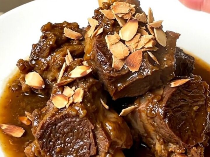 A close-up of slow-cooked tender lamb chunks in a rich glossy sauce with prunes.