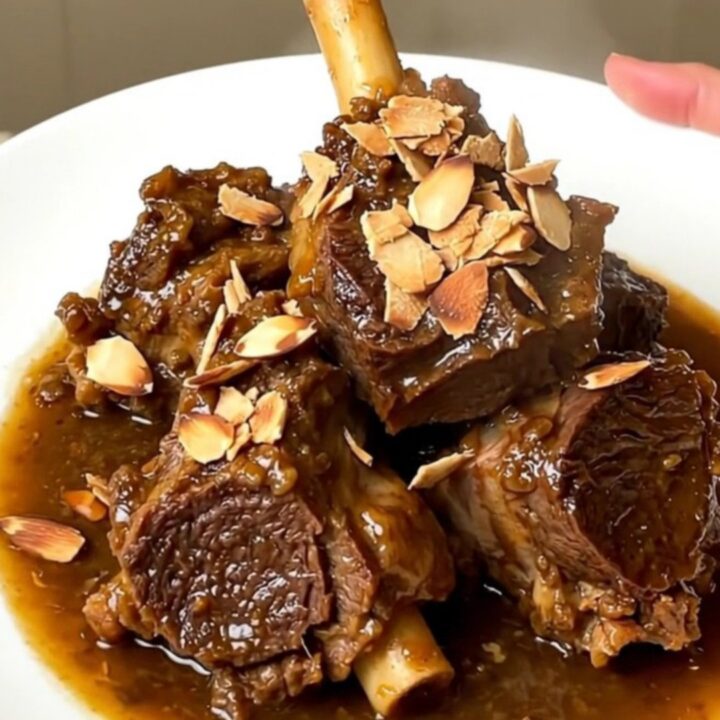 A close-up of slow-cooked tender lamb chunks in a rich glossy sauce with prunes.