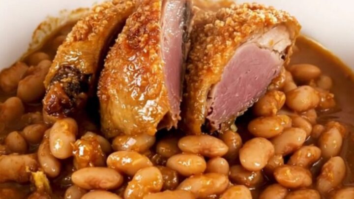 A rustic, steaming bowl of traditional cassoulet featuring golden duck confit, sausages, and tender white beans.