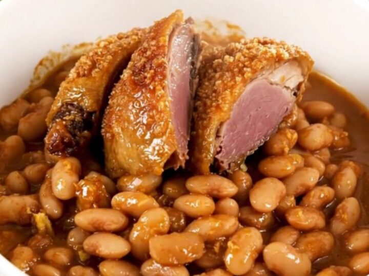 A rustic, steaming bowl of traditional cassoulet featuring golden duck confit, sausages, and tender white beans.