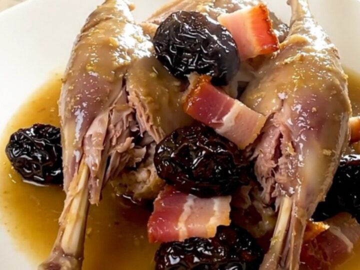 A plate of slow-cooked rabbit with prunes and bacon, showing tender meat and a glossy sauce.
