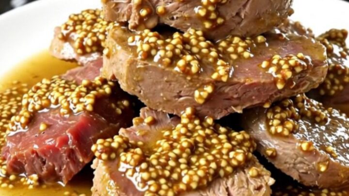 A steaming plate of tender veal tendrons coated in a rich, creamy wholegrain mustard sauce with soft carrots and onions.