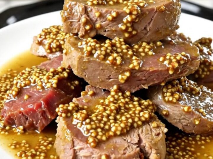 A steaming plate of tender veal tendrons coated in a rich, creamy wholegrain mustard sauce with soft carrots and onions.