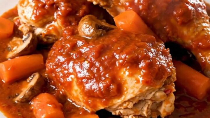 A close-up of a steaming, glossy plate of Chicken Marengo with visible mushrooms and carrots in a rich red tomato sauce.