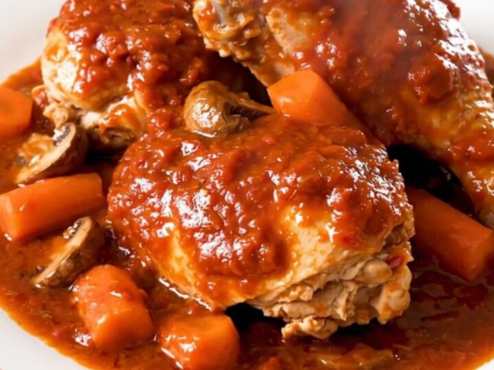 A close-up of a steaming, glossy plate of Chicken Marengo with visible mushrooms and carrots in a rich red tomato sauce.