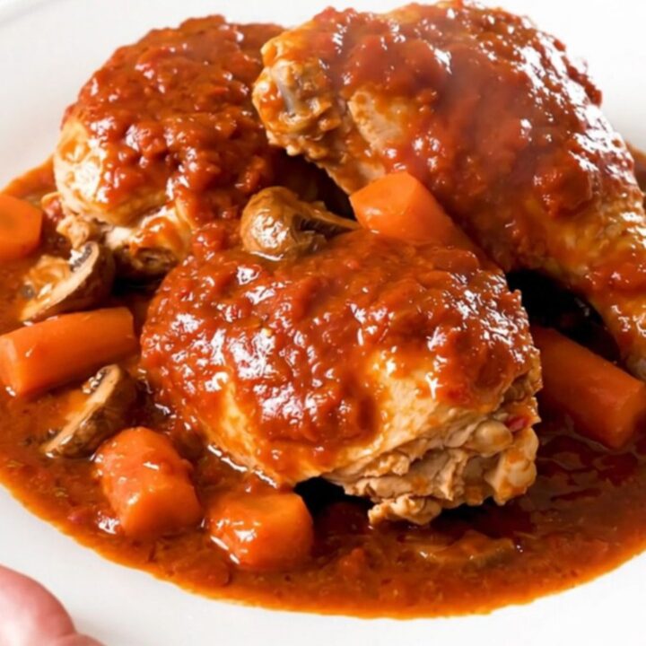 A close-up of a steaming, glossy plate of Chicken Marengo with visible mushrooms and carrots in a rich red tomato sauce.