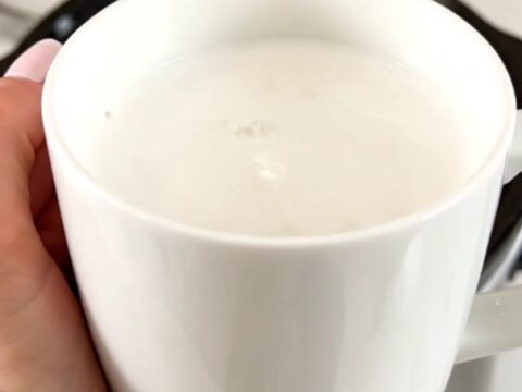 A white ceramic mug filled with creamy white hot chocolate on a white speckled countertop.