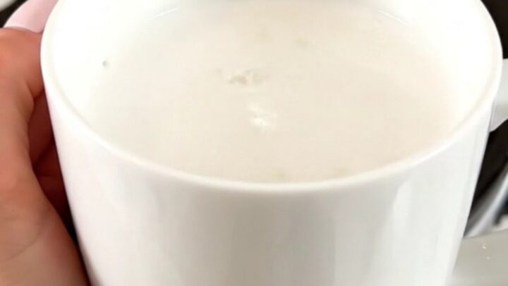 A white ceramic mug filled with creamy white hot chocolate on a white speckled countertop.