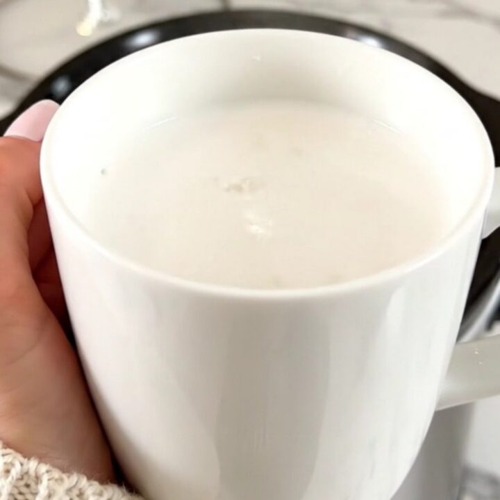 A white ceramic mug filled with creamy white hot chocolate on a white speckled countertop.