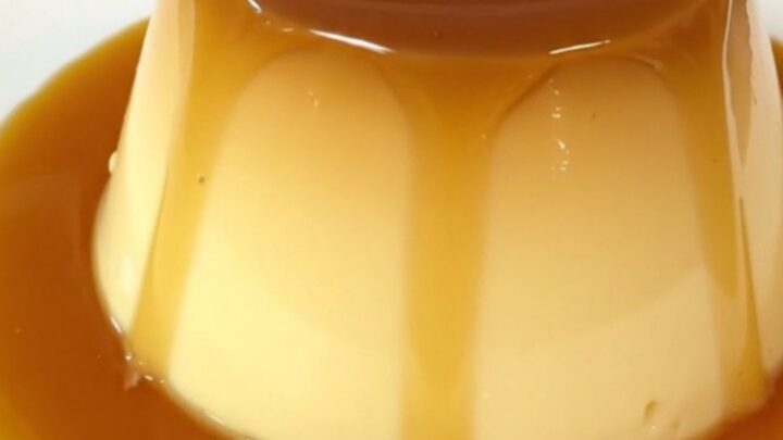 A top-down view of a black slow cooker insert filled with a smooth, golden custard mixture topped with caramel.