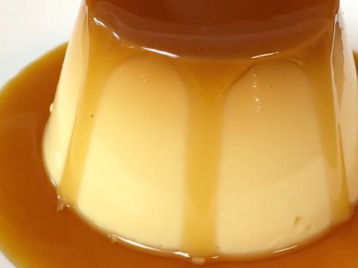 A top-down view of a black slow cooker insert filled with a smooth, golden custard mixture topped with caramel.