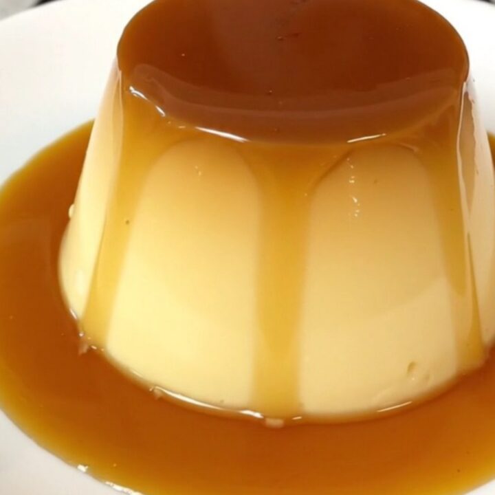 A top-down view of a black slow cooker insert filled with a smooth, golden custard mixture topped with caramel.