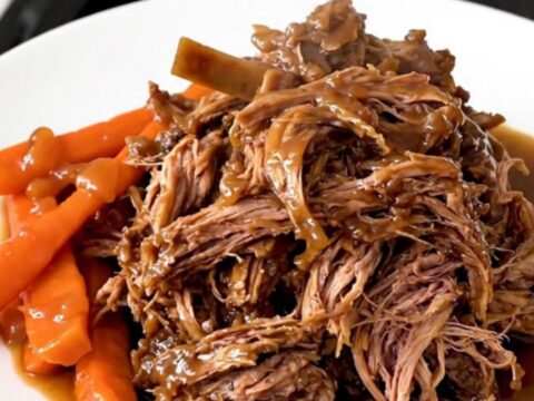 A rustic, slow-cooked lamb shoulder served in a white bowl with tender carrots and onions, garnished with herbs.
